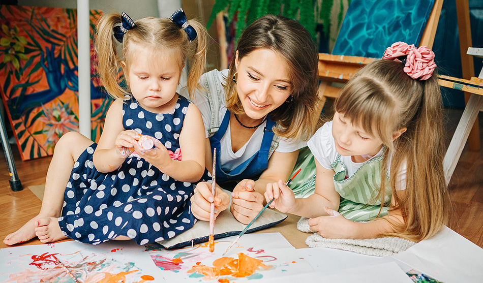 An educator painting on the floor with two young children