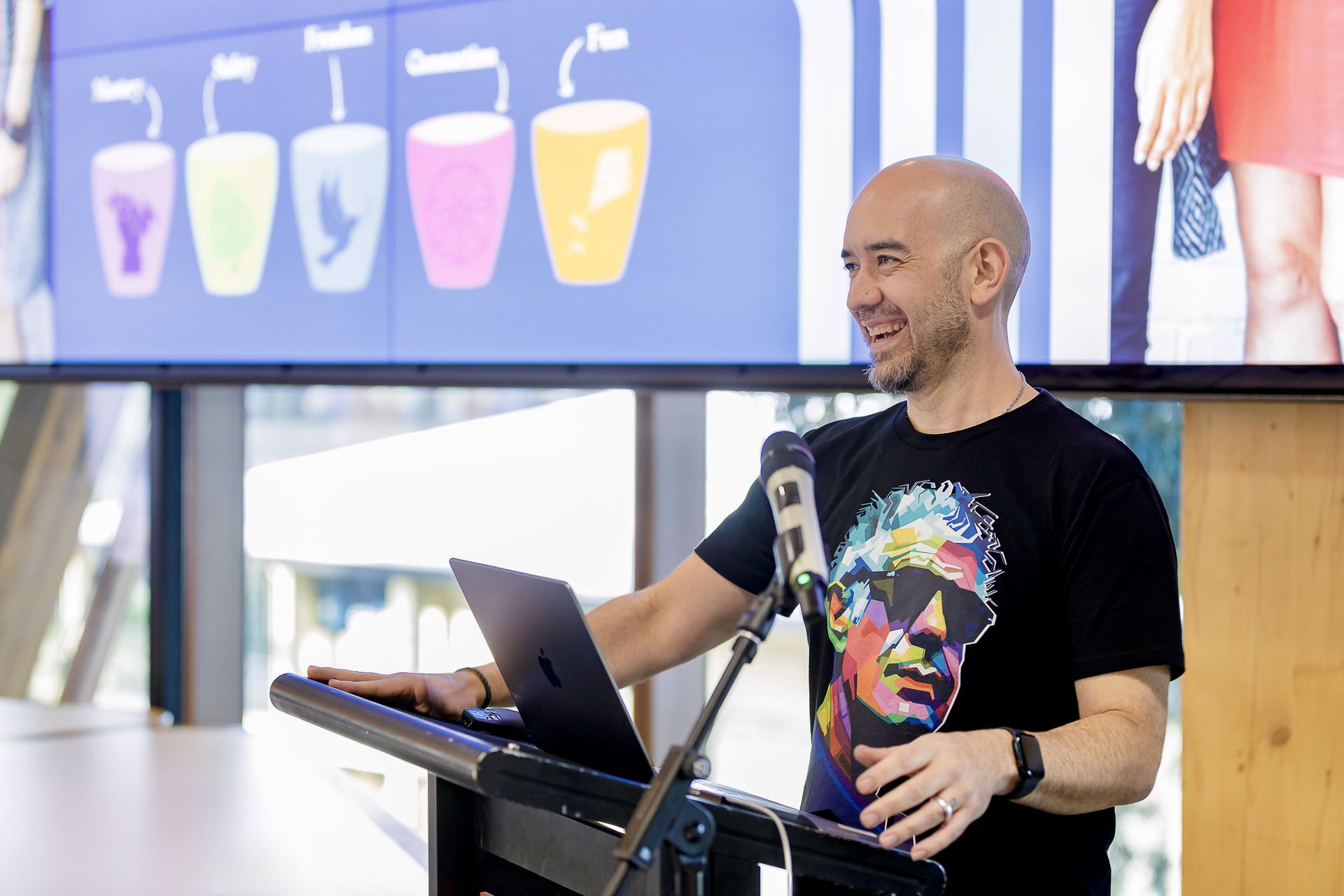Christopher Phoenix presenting at a lectern, with the five Phoenix Cups on the screen behind him